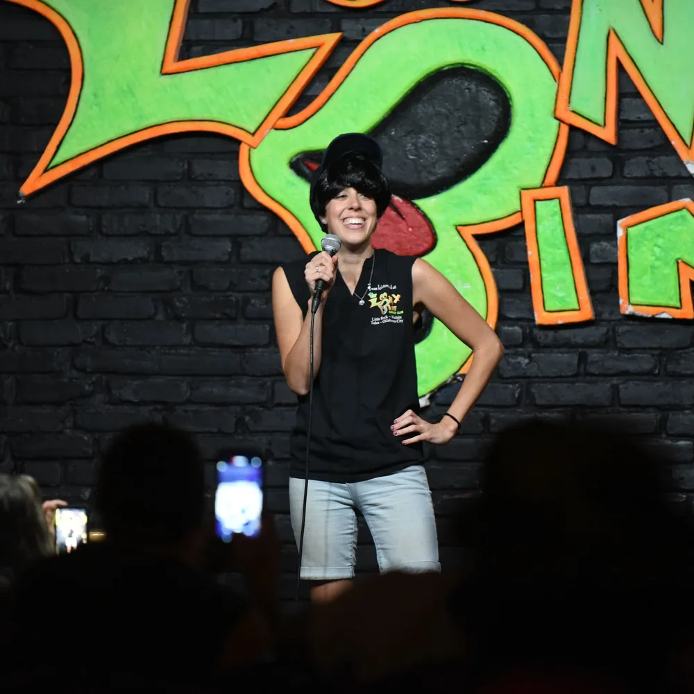 Guests at round tables laugh and clap as costumed performers take a bow on a small stage