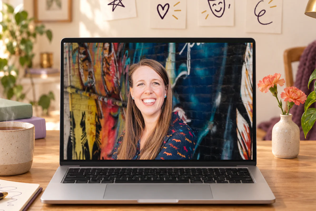 Hailey Jones smiling on a video call on an open laptop at a warm home desk with a mug of tea, a notebook and plants